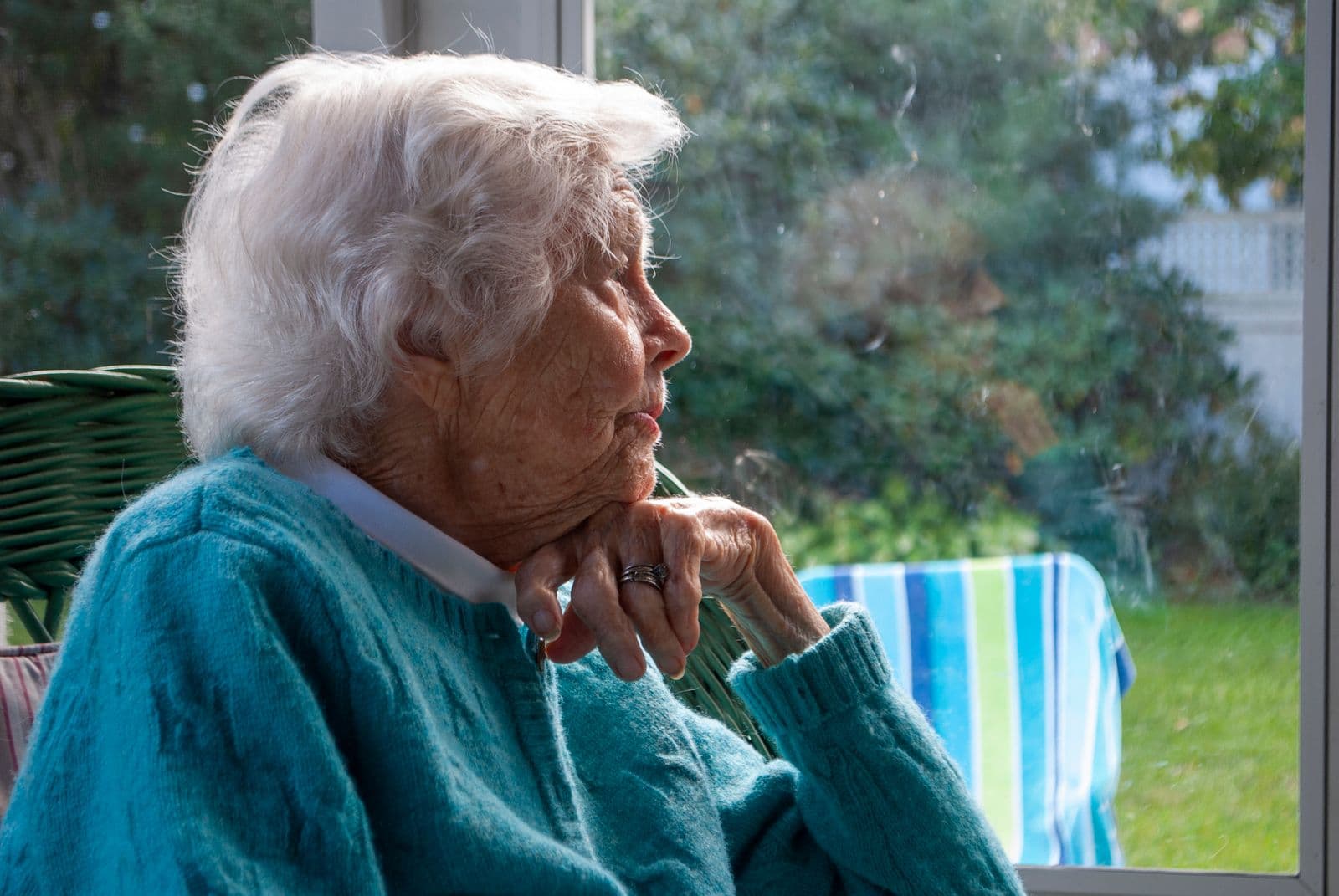 Elderly woman gazing thoughtfully out a bright window