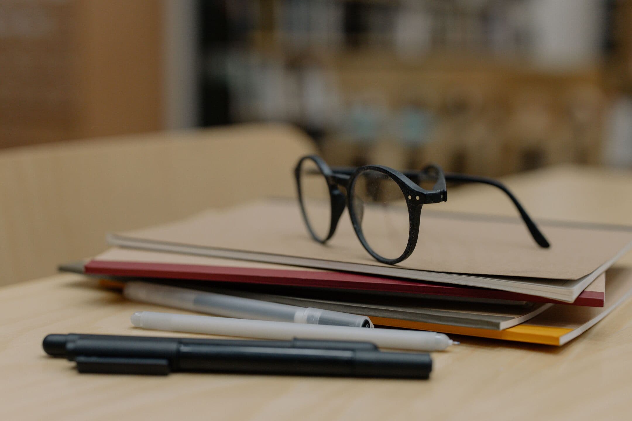 Round black glasses resting on a stack of kraft and red folders, with pens in front