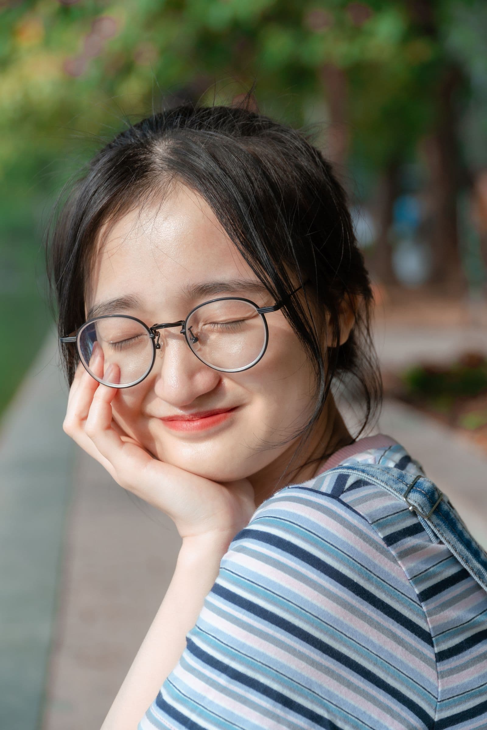 Smiling young woman in round eyeglasses outdoors among greenery