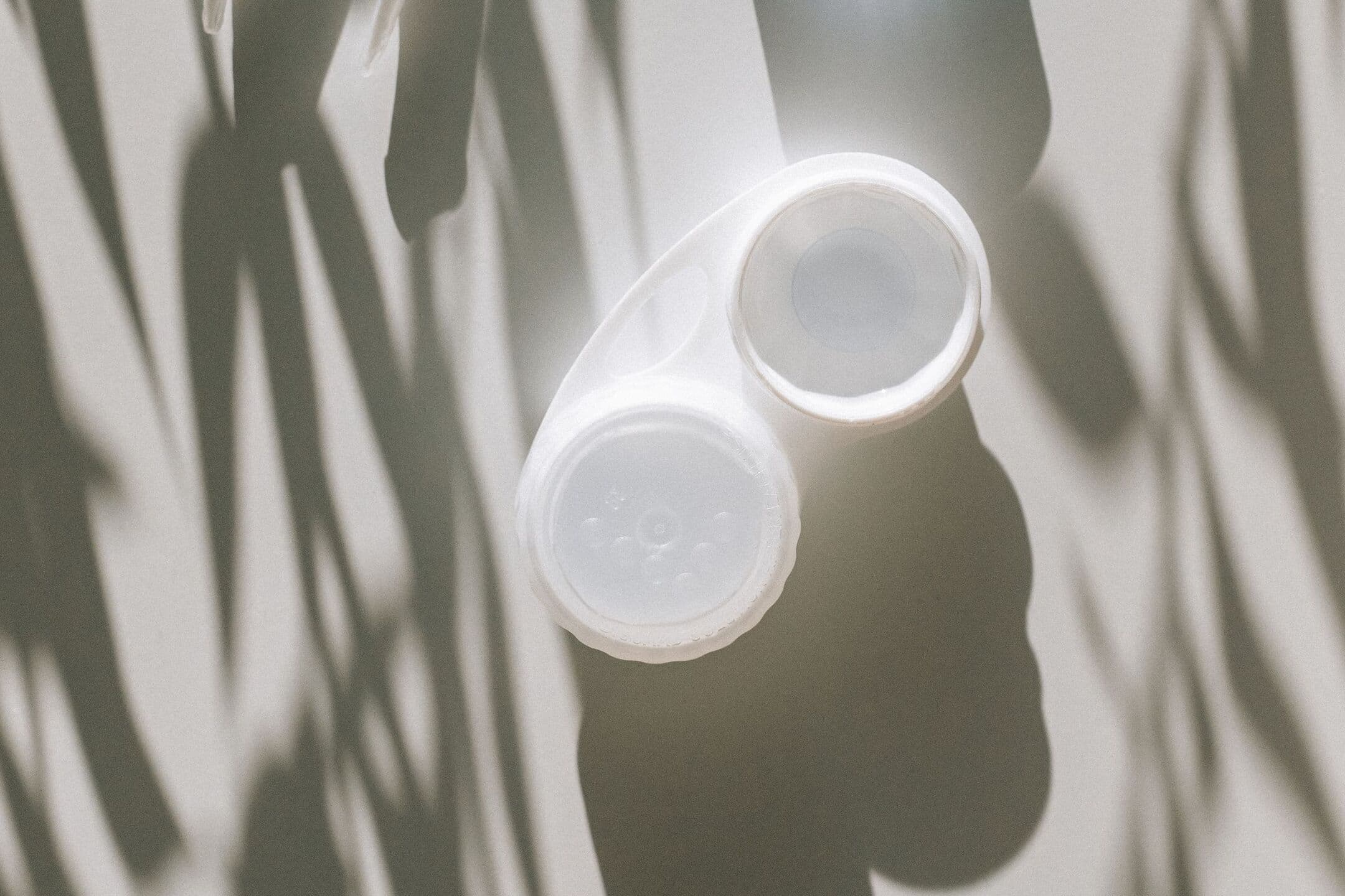 A white contact lens case on a pale surface, crossed by the shadows of leaves