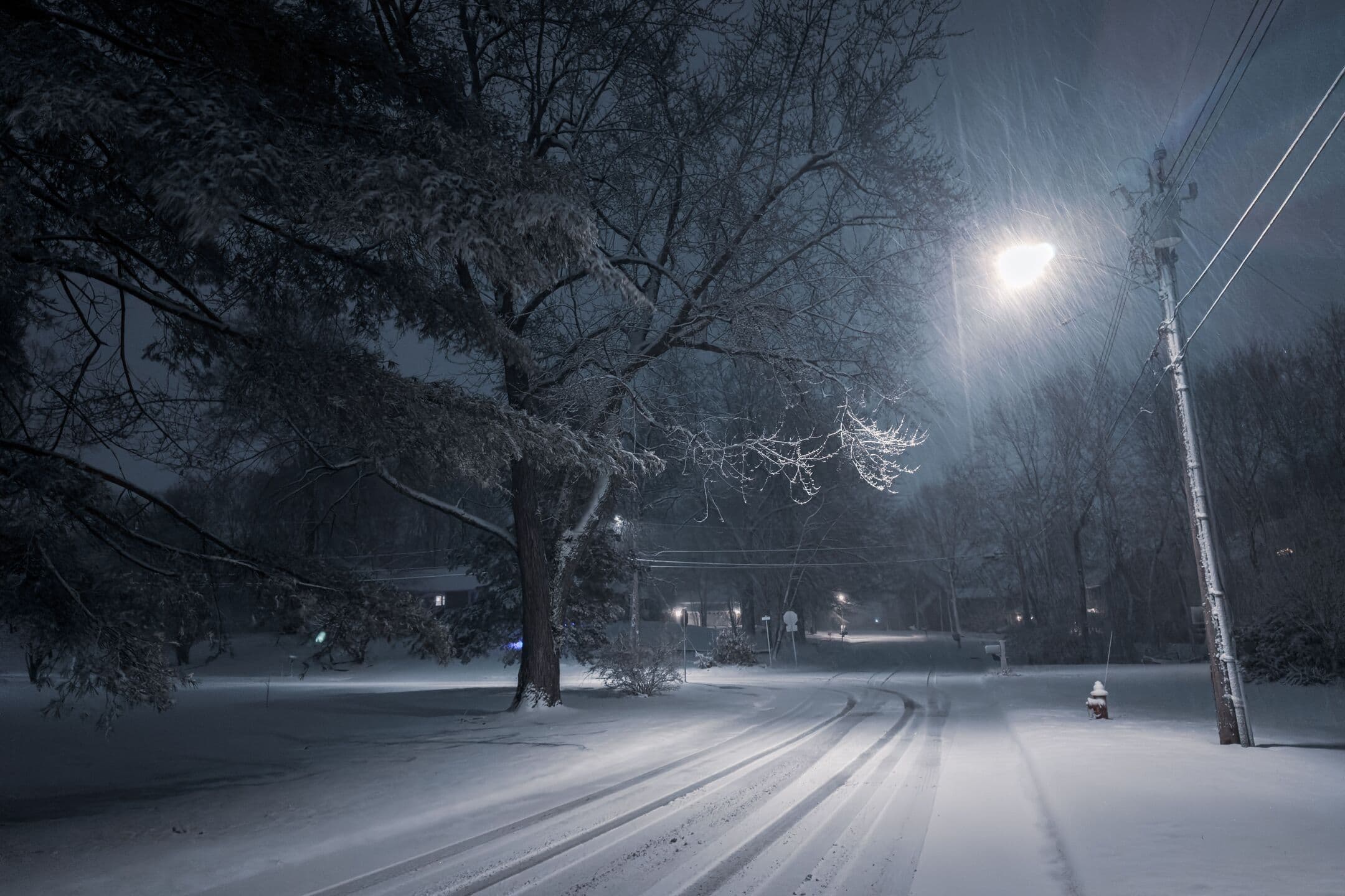 A quiet residential street at night under fresh snow, lit by a single streetlamp