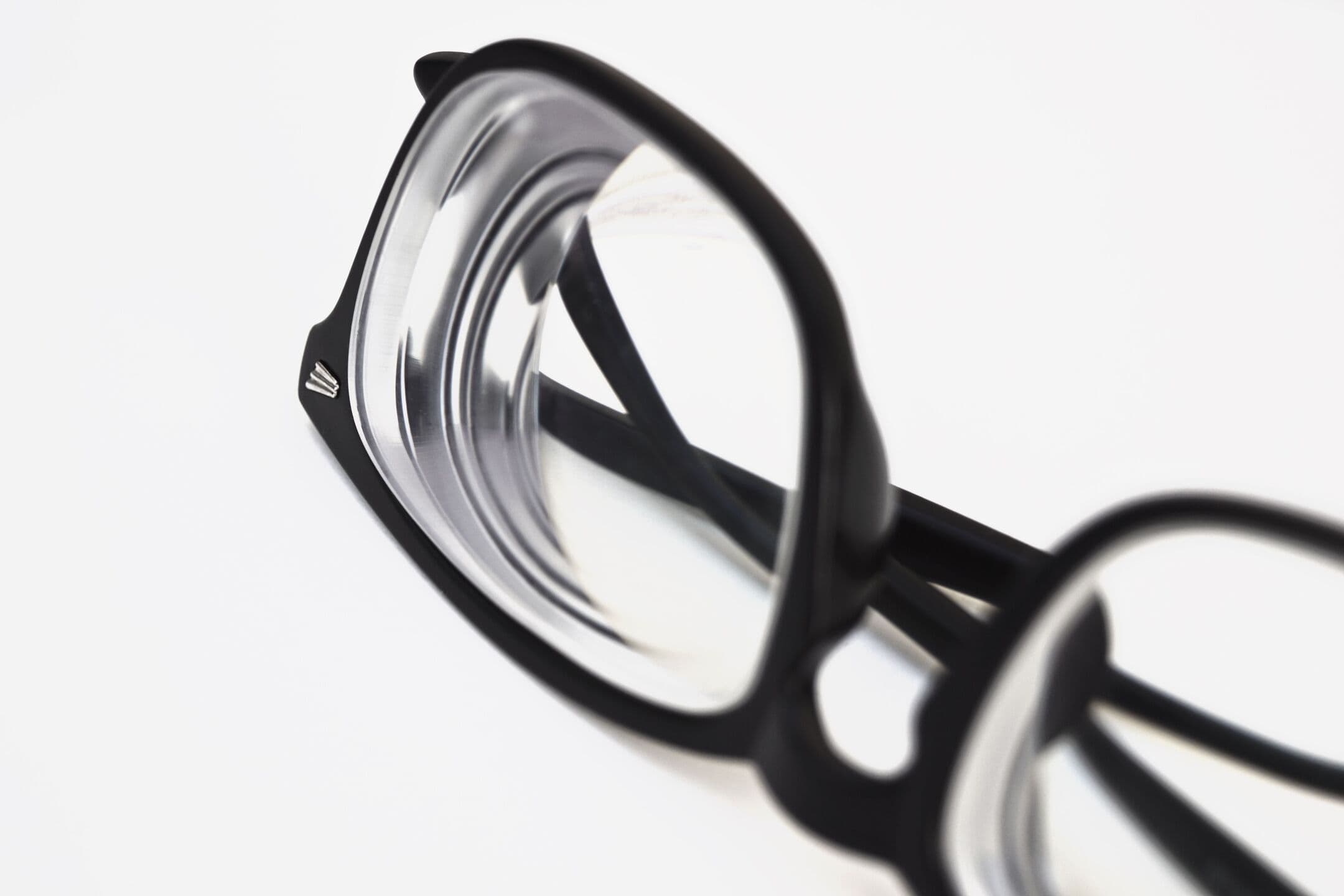 Close-up of black acetate glasses with thick, high-powered lenses, seen from the side on a white background